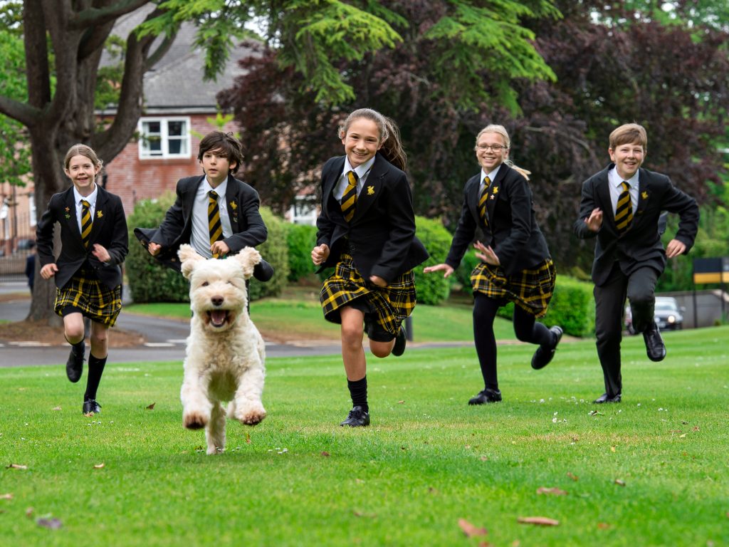 5 students running across the grass with a dog
