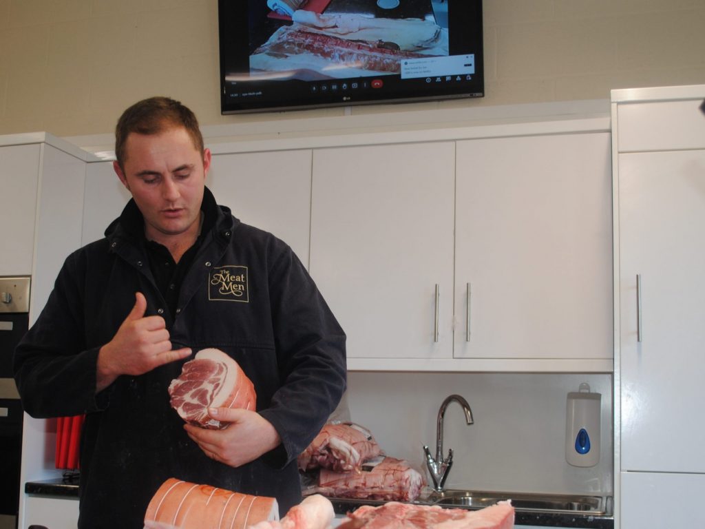 a man holding a piece of pork, talking about the different areas of the meat