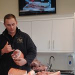 a man holding a piece of pork, talking about the different areas of the meat