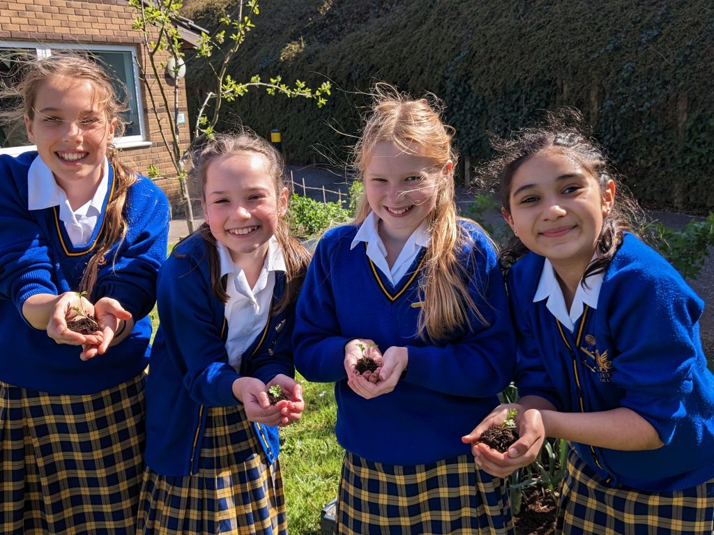 Queen's College students happily showing the seedlings they are about to plant in the ground