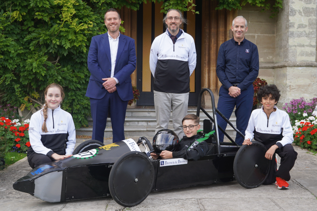 Queen's College Taunton Greenpower racing motorsports engineering team showing off their new kit sponsored by Brown & Brown, posing in the car, with Head of DT Mr Ben Higgs, and Brown & Brown.
