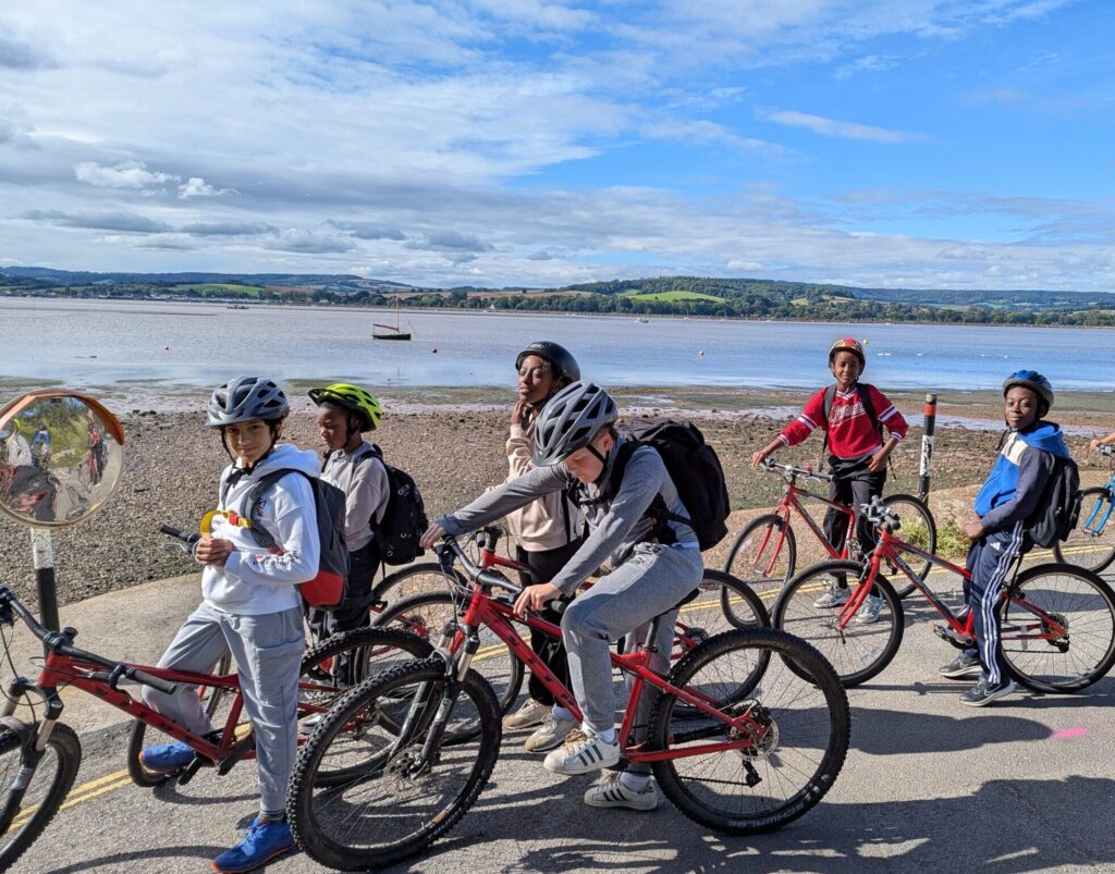 Some children on bicycles on a road next to the beach.