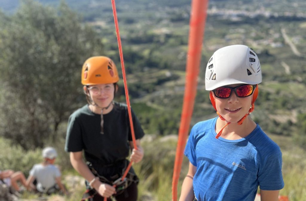2 pupils smiling wearing climbing helmets.